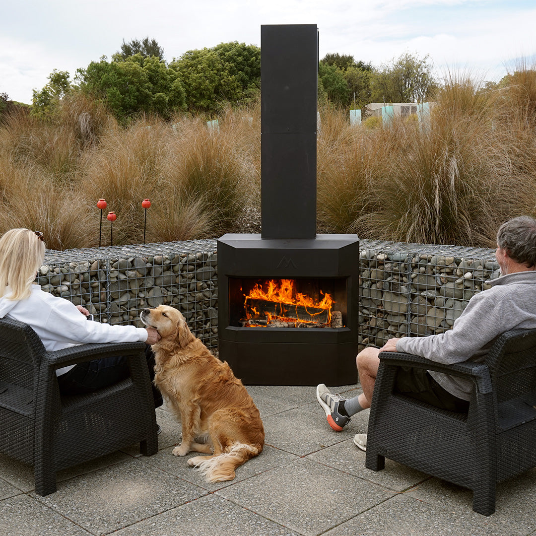Couple with dog hanging out in front of Pique Ascent outdoor fireplace