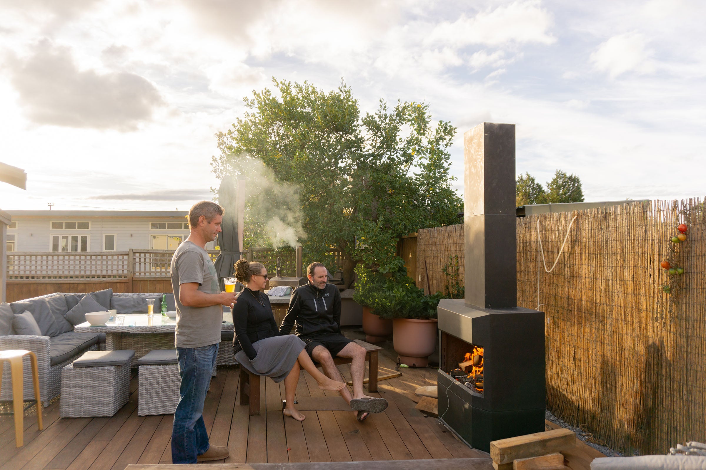 some friends sitting around a pique fires outdoor fireplace on timber deck