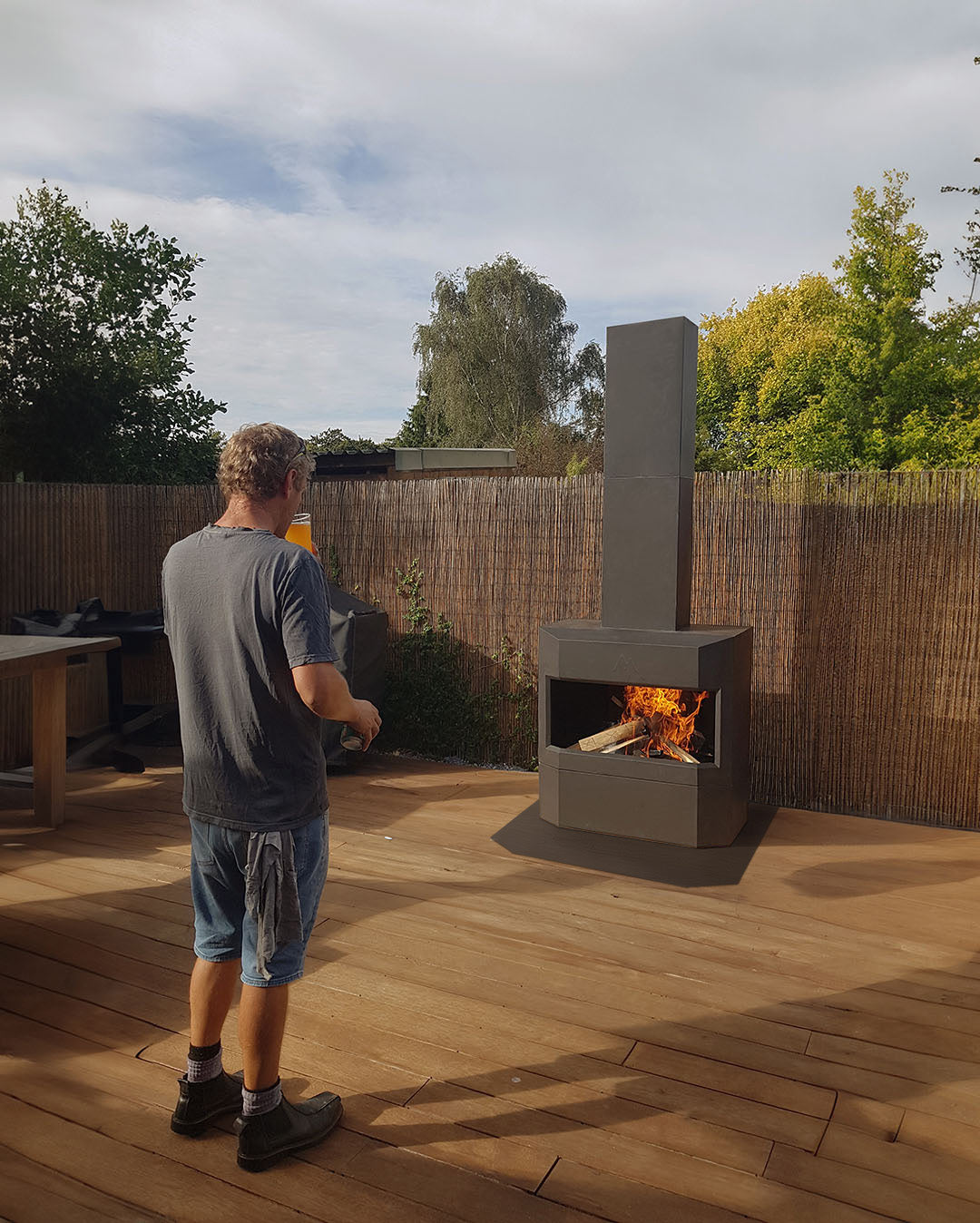 Man drinking beer on timber deck gazing into his Pique Ascent outdoor fireplace